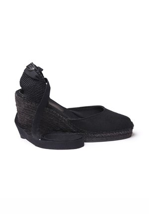 Juoda espadrilė su platforma, turinti audinio viršų ir pintą jutos kulną. Yra su apvalia nosimi ir juodu satino kulkšnies dirželiu su mazgo detalėmis.