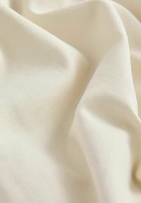 Tela de algodón beige con una textura suave, que presenta un sutil patrón acanalado y un suave caído, revelando ligeros pliegues y arrugas.