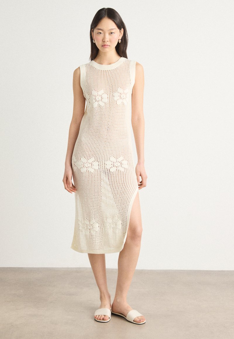 Knit cream-colored dress with a fitted design, sleeveless cut, side slit, and floral patterns integrated into the fabric texture.