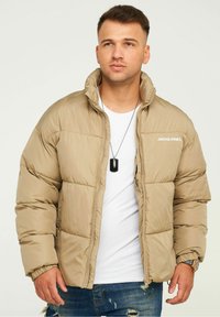 Beige Daunenjacke mit hohem Kragen, gepolstertem Design, Reißverschluss und elastischen Bündchen. Verfügt über ein Logo im linken Brustbereich.