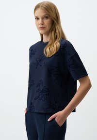 Marineblauwe sweatshirt met bloemenborduursel, korte mouwen en een relaxed fit; gecombineerd met bijpassende broek. Soepele textuur, casual ontwerp.