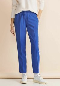 Lysblå byxor med en slät yta, med knäppning, sidofickor och rak bendesign. Matchas med vita sneakers.