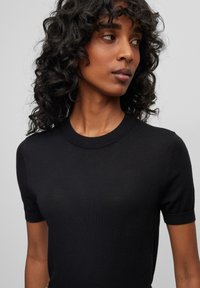 Maglione nero a maniche corte realizzato in maglia con collo a giro. Texture liscia e silhouette aderente, con una leggera lucentezza.