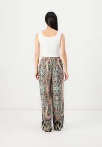 Wide-leg pants with a multicolored paisley pattern and a black background, paired with a fitted white tank top. Smooth fabric texture.