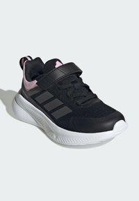Black athletic shoe with a mesh upper, pink accents, and three black stripes. Features a Velcro strap and cushioned white sole.