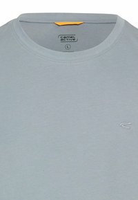 Lysegrå bomulds T-shirt med rund halsudskæring, prydet med et lille hvidt broderet logo på venstre bryst og et orange mærke ved halsen.
