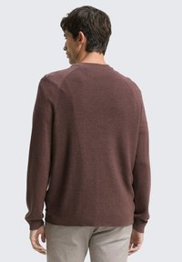 Bordeaux trui met een gestructureerd ribpatroon, lange mouwen, ronde hals en zijsplitten, weergegeven van achteren tegen een lichte achtergrond.