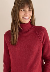 Maglione rosso a collo alto in maglia con dettagli a coste e una vestibilità comoda. Presenta maniche lavorate e un corpo liscio, ideale per sovrapposizioni.