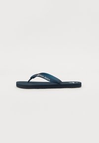 Sandal en tongs bleu marine avec une semelle texturée, des sangles incurvées et une marque 'Calvin Klein Jeans' sur la sangle supérieure. Matériau doux.