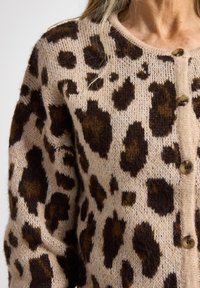 Cardigan à imprimé léopard en matériau tricot doux dans des tons beiges et marron, avec un col rond et des fermetures à boutons en bois.