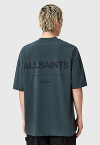 Tamsiai žalia didelio dydžio marškinėliai su ryškiu juodu tekstu "ALLSAINTS" ir "LONDON" ant nugaros, pagaminti iš lygaus medvilninio audinio ir trumpomis rankovėmis.