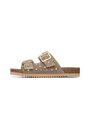 Sandalia tipo slide de ante marrón con dos correas ajustables con hebillas. Presenta tachuelas decorativas en la parte superior y una suela texturizada y duradera.