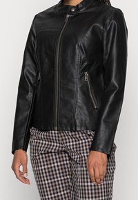Black faux leather jacket with a high collar, front zip closure, and zippered side pockets. Smooth texture, fitted design, and sleek silhouette.