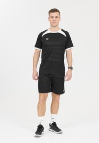 Svart sporttröja med vita detaljer, strukturerad tyg, ihop med svarta shorts och svarta löparskor. Vita sportstrumpor synliga.