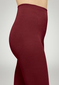 Bordeaux leggings med en glat, struktureret overflade. Elastisk taljebånd og tætsiddende design, der fremhæver diskrét formning langs hofter og l�år.