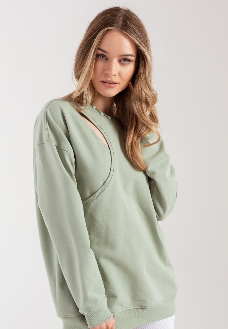 Jasnozielona bluza z unikalnym asymetrycznym wycięciem na klatce piersiowej, wykonana z miękkiego materiału i charakteryzująca się luźnym fasonem.