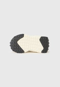 Såle på sko med en teksturert, kremfarget bunn med svarte gummidetaljer og hevede sirkulære mønstre for grep.