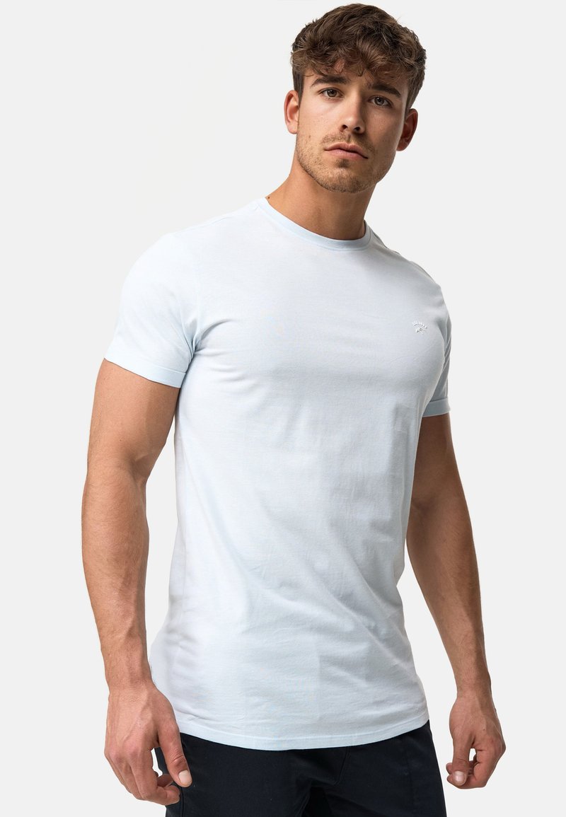 Tricou din bumbac de culoare albastru deschis, cu guler rotund, croială slim, mâneci scurte și un mic logo pe piept. Textură netedă, design minim.