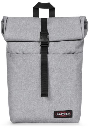 Mochila gris de tipo roll-top con cierre de cinta negra, tejido texturizado, bolsillo frontal y logo de Eastpak en la esquina inferior derecha.
