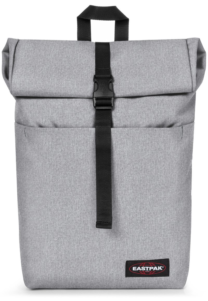 Mochila gris de tipo roll-top con cierre de cinta negra, tejido texturizado, bolsillo frontal y logo de Eastpak en la esquina inferior derecha.