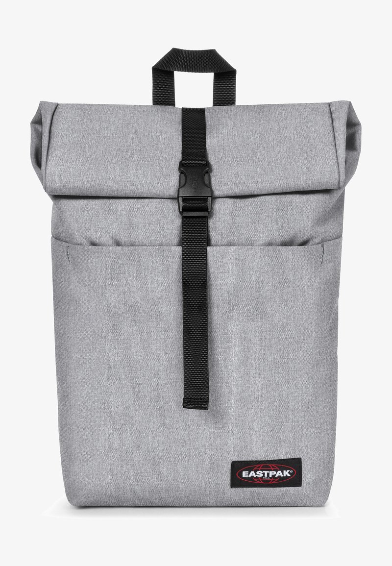 Sac à dos à rabat gris avec fermeture à sangle noire, tissu texturé, poche avant et logo Eastpak en bas à droite.