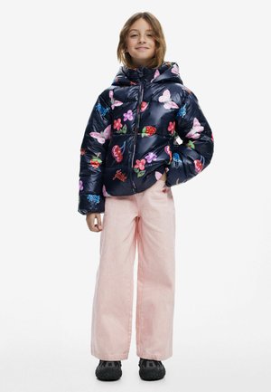 Puffig marinblå jacka med blommönster och fruktmönster, kombinerad med ljusrosa vida byxor och svarta sneakers. Har en huva och dragkedja.