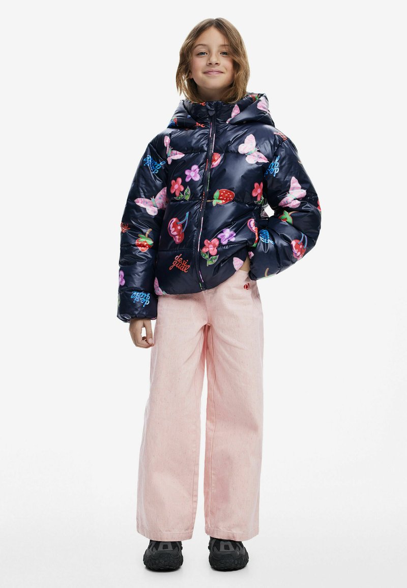 Puffig marinblå jacka med blommönster och fruktmönster, kombinerad med ljusrosa vida byxor och svarta sneakers. Har en huva och dragkedja.