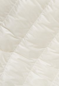 Tessuto bianco trapuntato con una finitura brillante, caratterizzato da cuciture diagonali e sezioni imbottite, creando un aspetto morbido e texturizzato.
