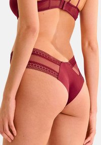 Ensemble de lingerie bourgogne avec des détails en filet transparent et en dentelle ; string taille basse avec des accents en dentelle sur les côtés et un tissu lisse.