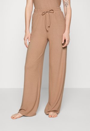 Wide-leg pants in a flat, tan knit fabric with an elastic waistband and drawstring tie. Features a smooth texture and relaxed fit.