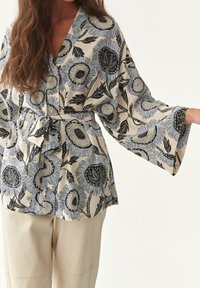 Top avvolgente in tessuto crema con motivo floreale blu e nero. Caratterizzato da maniche ampie e una cintura coordinata in vita.