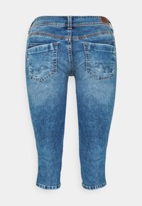 Jean capri en denim bleu, avec une coupe flatteuse, des détails cousus et deux poches arrière. Le tissu présente une texture lisse légèrement délavée.