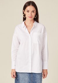 Witte blouse met lange mouwen van zachte stof, met een knoopsluiting aan de voorkant, een klassieke kraag en een enkele borstzak. Eenvoudig, strak ontwerp.