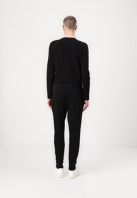 Black long-sleeve shirt and matching trousers, both featuring a fitted style. The outfit is paired with white sneakers on a plain background.