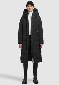 Giacca a vento nera con colletto alto, cappuccio ampio, tasche con zip e lunghezza lunga; presenta un tessuto strutturato e trapuntato con dettagli del logo.