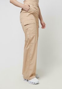 Bež hlače cargo kroja z ravnimi hlačnicami, z bočnimi žepi in zadrgo na predelu sprednjice. Iz lahkega materiala, kombinirane z belimi športnimi copati.