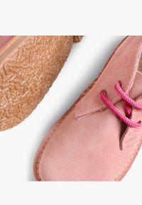 Zapato de ante rosa con cordones rosa brillante y una suela de goma marrón claro con textura, mostrado desde ángulos superior e inferior.