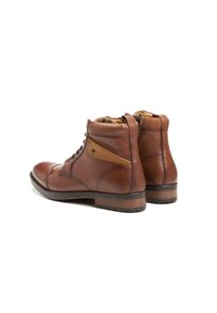 Bottes chelsea en cuir marron avec une finition texturée, à lacets, et un panneau contraste en tan. Semelle en caoutchouc durable avec un léger talon.