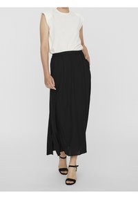 Falda maxi negra con un corte relajado, cinturilla elástica y aberturas laterales, combinada con una blusa blanca sin mangas y tacones negros con tiras.
