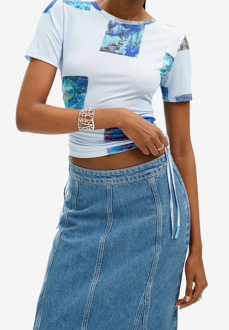 Top corto azul claro con estampados de cuadrados coloridos, combinado con una falda de mezclilla de corte recto y detalle de cordón en el costado.