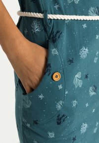 Turkusowa sukienka z nadrukiem koralowców i morskich stworzeń, z linowym paskiem i drewnianym guzikiem na kieszeni. Miękki, przewiewny materiał.