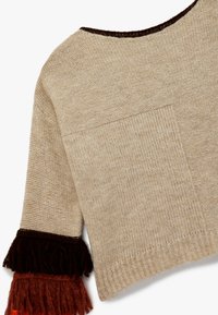 Pull en maille beige avec un large col, une grande poche avant et des manches à franges dans des tons de marron foncé, rouille et orange.