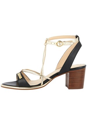 Sandalias de tacón en negro y dorado con diseño de tira en T y tacón de bloque de madera. Presenta tiras cruzadas y un acento metálico en la parte superior.