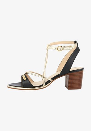 Sandalias de tacón en negro y dorado con diseño de tira en T y tacón de bloque de madera. Presenta tiras cruzadas y un acento metálico en la parte superior.