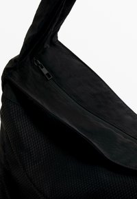 Zwarte tas van getextureerd materiaal met een gladde bovenklep en een ritssluiting. Het ontwerp is minimalistisch en functioneel.