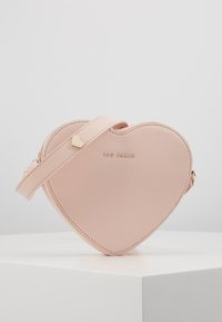 Torebka w kształcie serca w różowym kolorze, wykonana z gładkiej skóry, z złotym logo, gładką fakturą oraz odczepianym paskiem z małym złotym akcentem w kształcie serca.