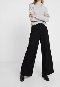 Grå långärmad topp med ett subtilt mönster på bröstet, kombinerad med högmidjade, vida svarta jeans och svarta ankelstövlar.