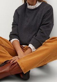 Sweatshirt gris foncé avec une coupe décontractée, encolure côtelée et manches retroussées, associé à un pantalon en velours côtelé orange et des bottes marron.