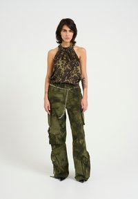 Top con collo all'americana verde scuro e stampa leopardata nera, abbinato a pantaloni cargo verde oliva con molteplici tasche e una cintura a catena in argento.