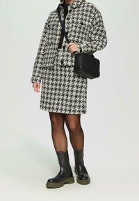 Chaqueta y falda con estampado de pata de gallo en blanco y negro, combinadas con botines negros de cuero y un pequeño bolso negro texturizado.